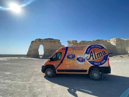 A colorful delivery van parked near a natural rock formation under a clear blue sky.