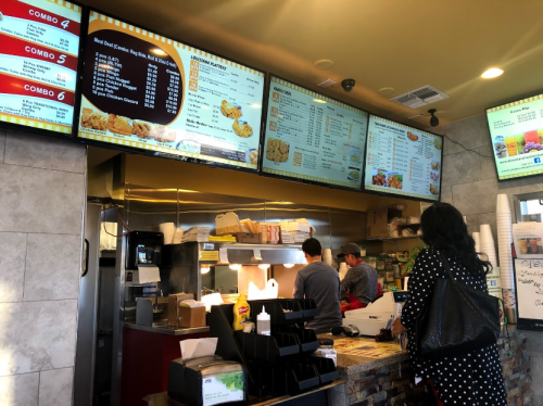 A busy fast-food restaurant interior with a menu board, customers ordering, and staff preparing food.