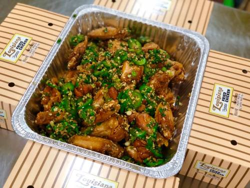 A tray of spicy chicken wings topped with green onions and peanuts, surrounded by striped takeout boxes.