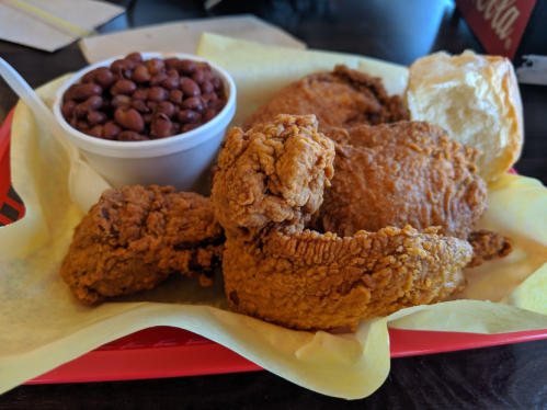 A red tray with fried chicken pieces, a biscuit, and a cup of black beans on a yellow napkin.