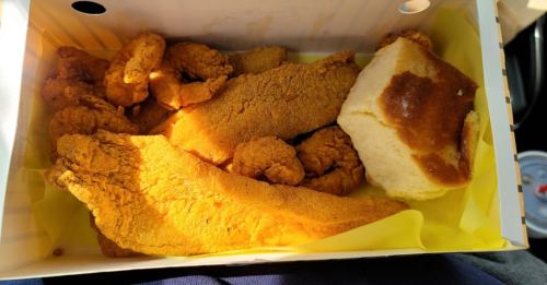 A takeout box filled with golden fried chicken pieces, fish fillets, and a soft roll.