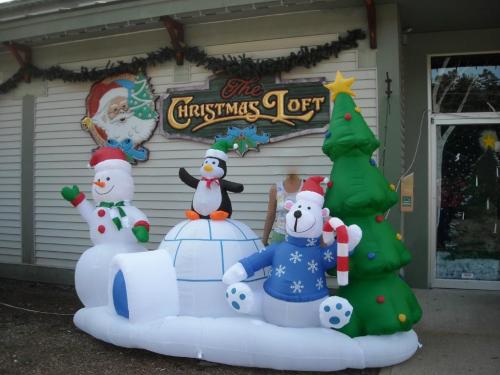 Inflatable Christmas decorations featuring a snowman, penguin, bear, and tree in front of a festive store sign.