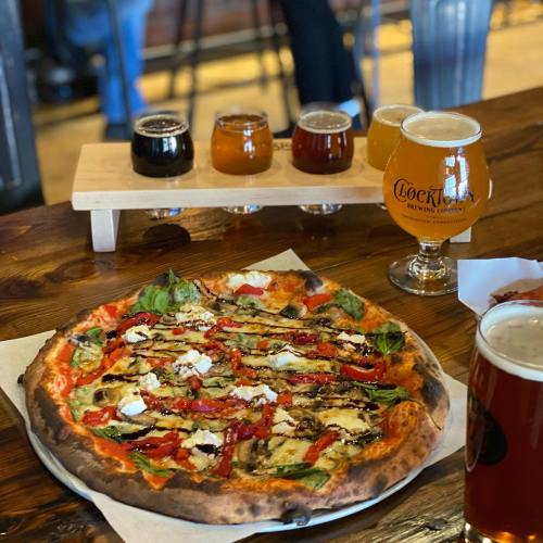 A delicious pizza topped with vegetables and cheese, accompanied by a flight of craft beers and a glass of beer.
