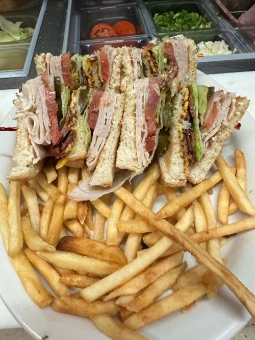 A large club sandwich stacked with meats and veggies, served with a side of golden French fries.