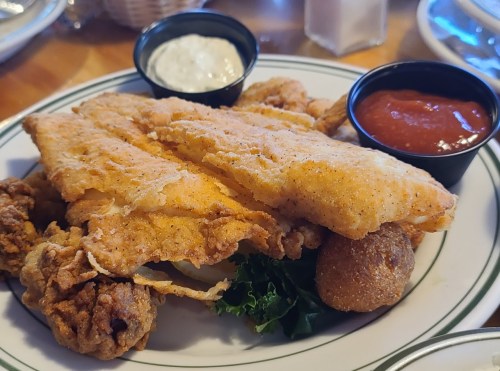 A plate of fried fish fillets, hushpuppies, and dipping sauces, served on a bed of lettuce.