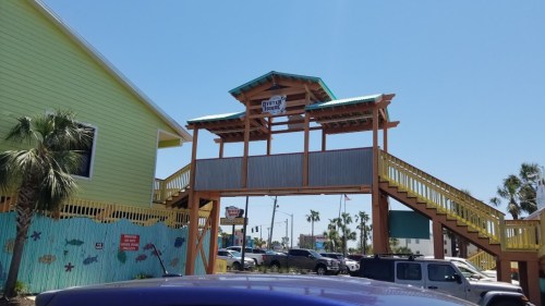 Colorful beachside structure with a wooden walkway, palm trees, and a clear blue sky in the background.