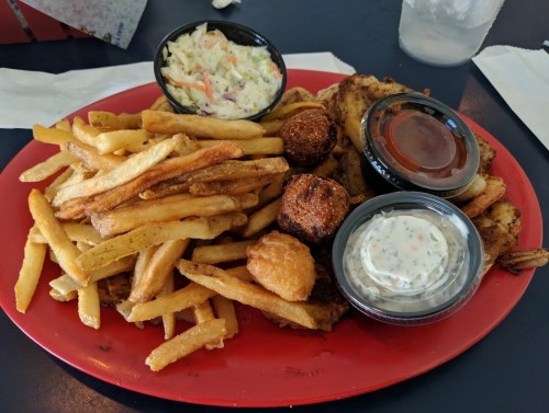 A red plate filled with fries, coleslaw, fried shrimp, and two dipping sauces.