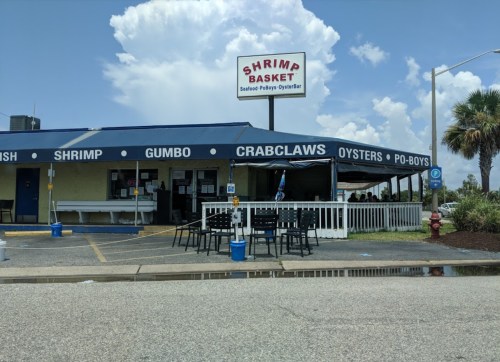 A seafood restaurant with a blue awning, featuring a sign that reads "Shrimp Basket" and outdoor seating.