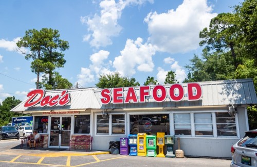 A seafood restaurant named "Doc's Seafood" with a bright red sign, surrounded by trees and a clear blue sky.