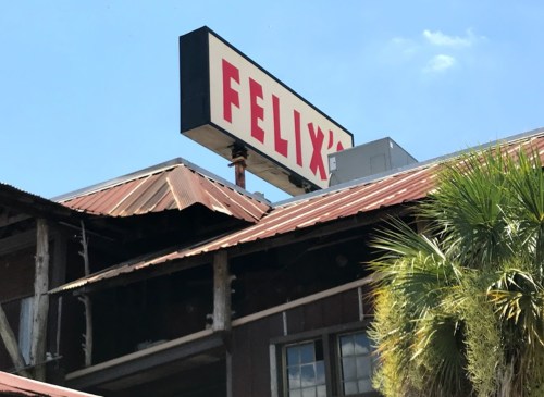 Sign for "Felix's" on a building with a rusted roof and palm trees in the foreground under a clear blue sky.