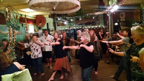 A lively gathering of people dancing and enjoying music in a warmly lit, festive restaurant setting.