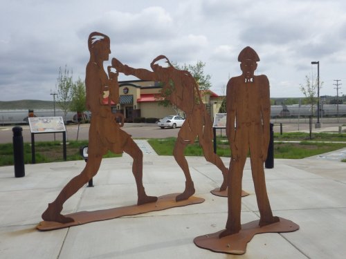 Three metal sculptures depict boxers in action, with one figure standing still, set against a cloudy sky.