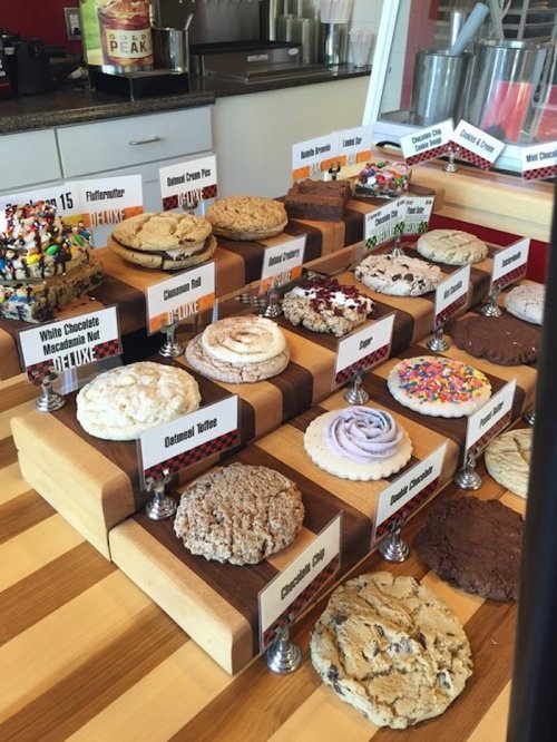 A display of various cookies on wooden stands, each labeled with names and flavors, showcasing colorful toppings.