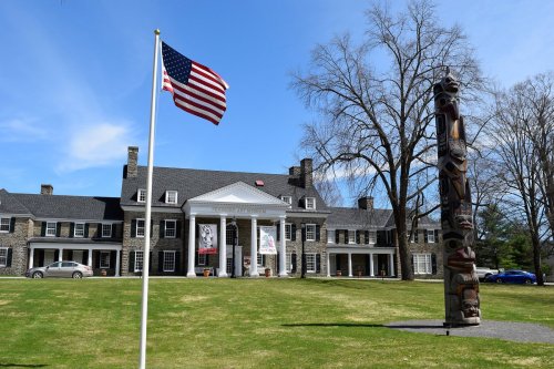 A large stone building with a flagpole and totem pole in front, set against a clear blue sky.