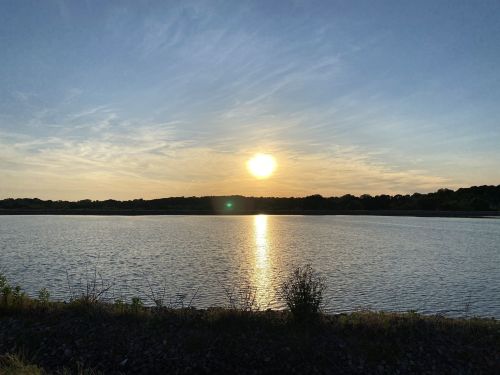 Sunset over a calm lake, with reflections on the water and a clear sky filled with wispy clouds.