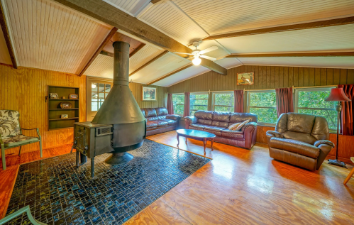 Cozy living room with a wood stove, leather sofas, and large windows, featuring wooden beams and a warm atmosphere.