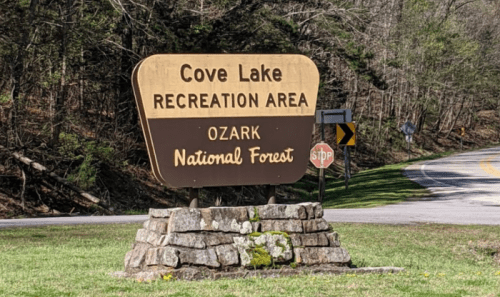 Sign for Cove Lake Recreation Area in Ozark National Forest, with a stone base and surrounding greenery.