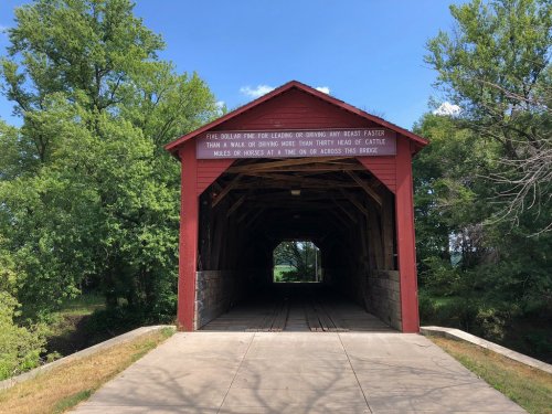A red covered bridge with a sign, surrounded by green trees and a clear blue sky.