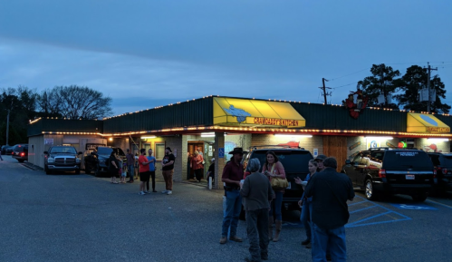 A lively restaurant exterior at dusk, with people gathered outside and warm lights illuminating the entrance.