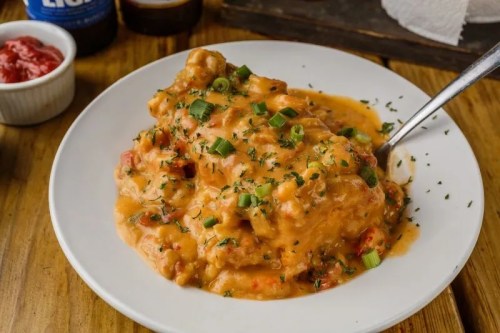 A plate of creamy chicken smothered in sauce, garnished with green onions, served with a side of sauce.