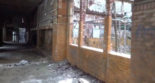 Abandoned building interior with crumbling brick walls and debris scattered on the floor, illuminated by natural light.