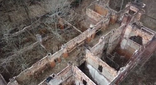 Aerial view of overgrown ruins with crumbling walls and trees, showcasing nature reclaiming an abandoned structure.