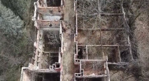 Aerial view of abandoned, crumbling building ruins surrounded by overgrown trees and vegetation.