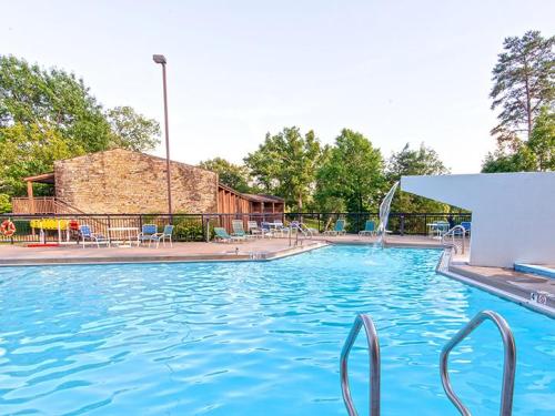 A clear blue swimming pool with a waterfall feature, surrounded by lounge chairs and trees in the background.