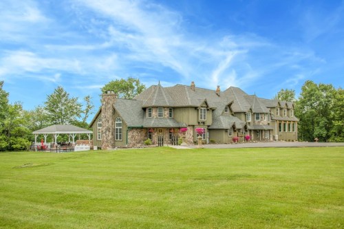 A large, elegant green mansion with a gazebo, surrounded by lush grass and trees under a blue sky.