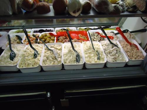 A display of various salads and toppings in containers, with serving spoons, arranged on a counter.