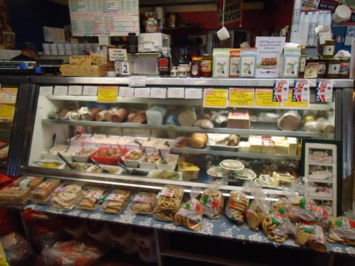 A colorful display of various cheeses, meats, and snacks in a deli case, with labels and packaged goods in front.