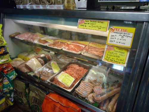 A display case filled with various meats, including sausage patties, ground meat, and packaged cuts, with price signs.
