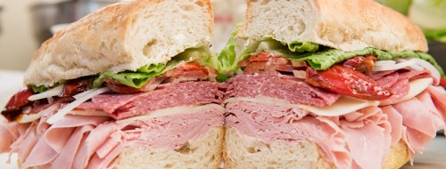 A freshly cut sandwich filled with layers of meats, cheese, lettuce, and tomatoes on a crusty bread.