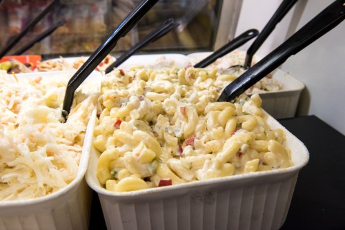 A serving dish of creamy macaroni salad with diced vegetables and black serving spoons.