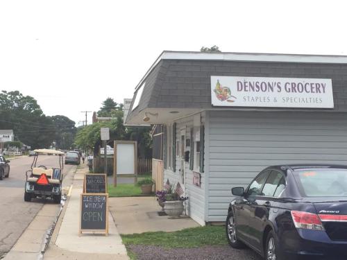 A small grocery store with a sign reading "Denson's Grocery" and an open window, parked cars and a golf cart nearby.