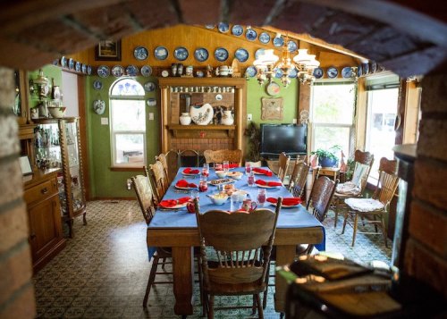 A cozy dining room with a large wooden table set for a meal, surrounded by vintage decor and blue plates on the walls.