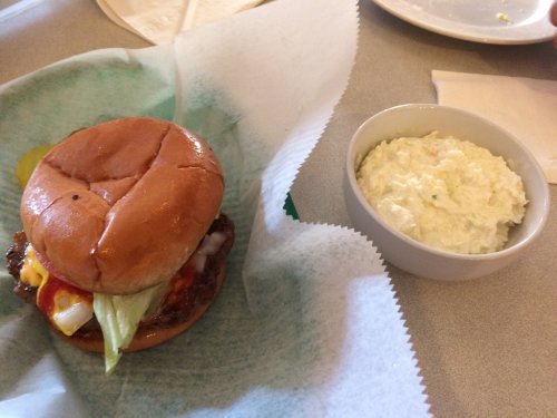 A hamburger with lettuce, pickles, and condiments next to a bowl of coleslaw on a green-lined plate.
