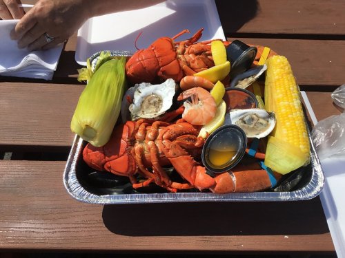 A seafood platter featuring lobster, shrimp, oysters, corn, and lemon, served in a foil tray on a wooden table.