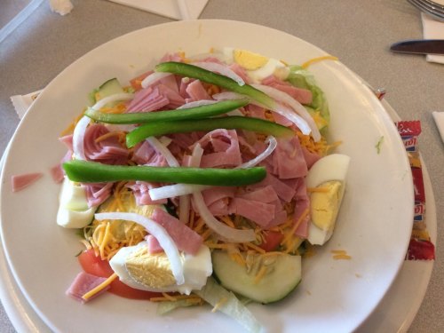 A colorful salad topped with ham, green peppers, onions, hard-boiled eggs, and shredded cheese on a bed of lettuce and tomatoes.