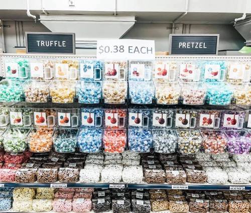 A colorful display of various popcorn flavors in clear containers, labeled with prices.