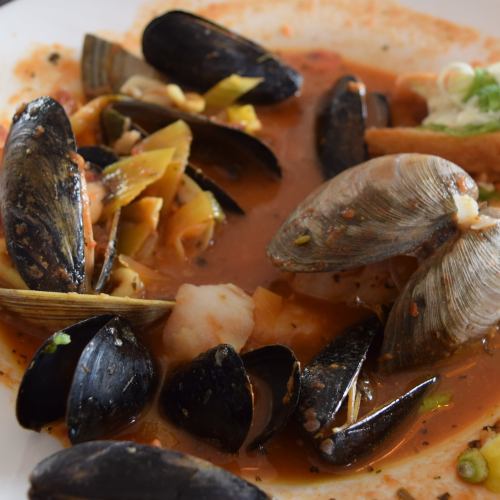 A close-up of a seafood dish featuring mussels, clams, shrimp, and vegetables in a rich, flavorful broth.