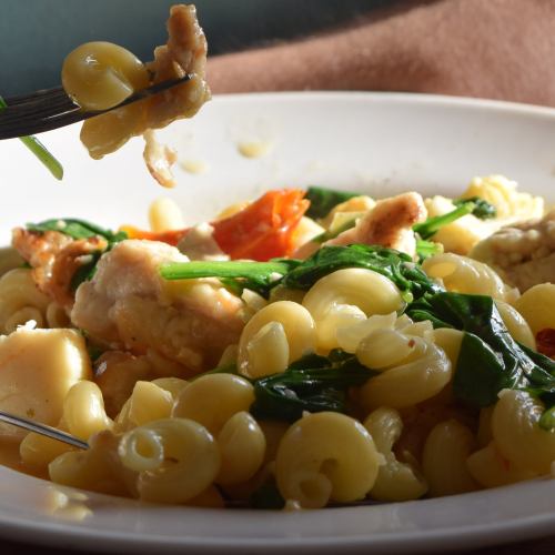 A close-up of a fork lifting pasta with chicken and spinach from a bowl, illuminated by natural light.