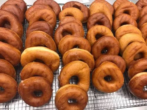 A tray of freshly made donuts, arranged in rows, showcasing a variety of golden-brown and light-colored pastries.