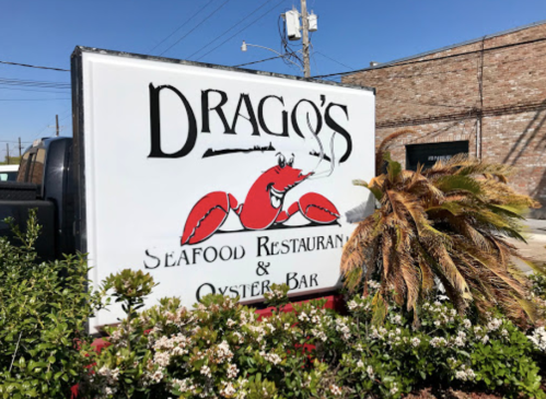 Sign for Drago's Seafood Restaurant & Oyster Bar featuring a red lobster graphic and surrounded by greenery.