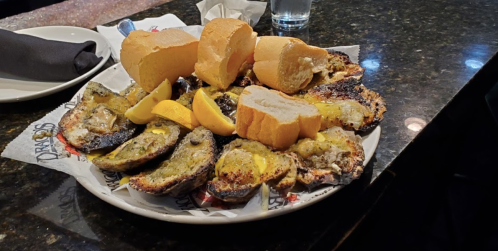 A platter of grilled oysters with lemon wedges and slices of bread on a dark countertop.
