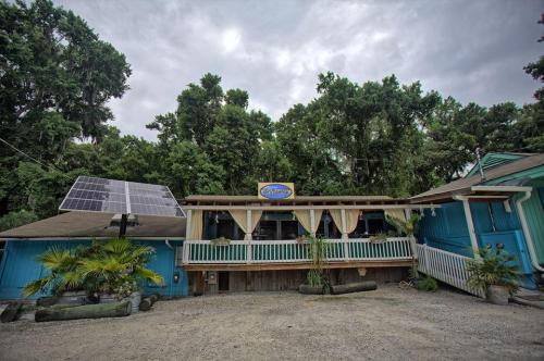 A colorful building with a porch, surrounded by trees, featuring solar panels and tropical plants in the foreground.