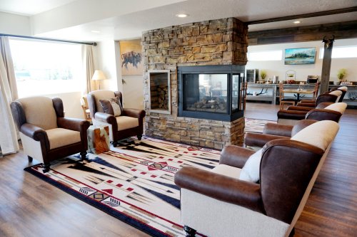 Cozy living room with a stone fireplace, comfortable chairs, and a patterned rug, creating a warm atmosphere.