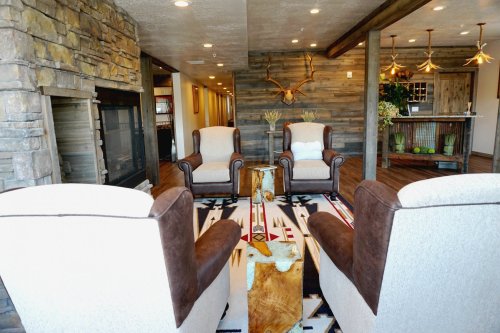 Cozy living area with two armchairs, a stone fireplace, wooden accents, and a patterned rug. Warm, inviting atmosphere.