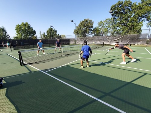 A group of people playing tennis on outdoor courts, with two players at the net and others in the background.
