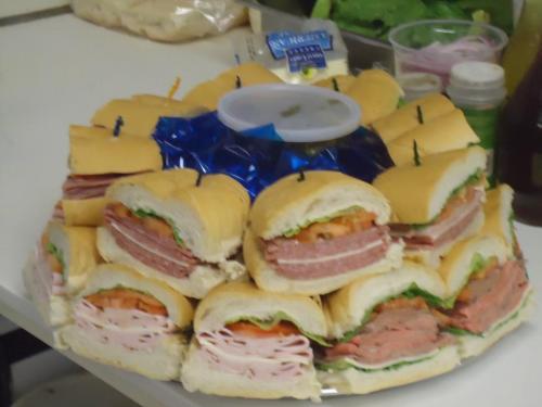 A platter of assorted sandwiches with layers of meats, lettuce, and tomatoes, arranged in a circular display.